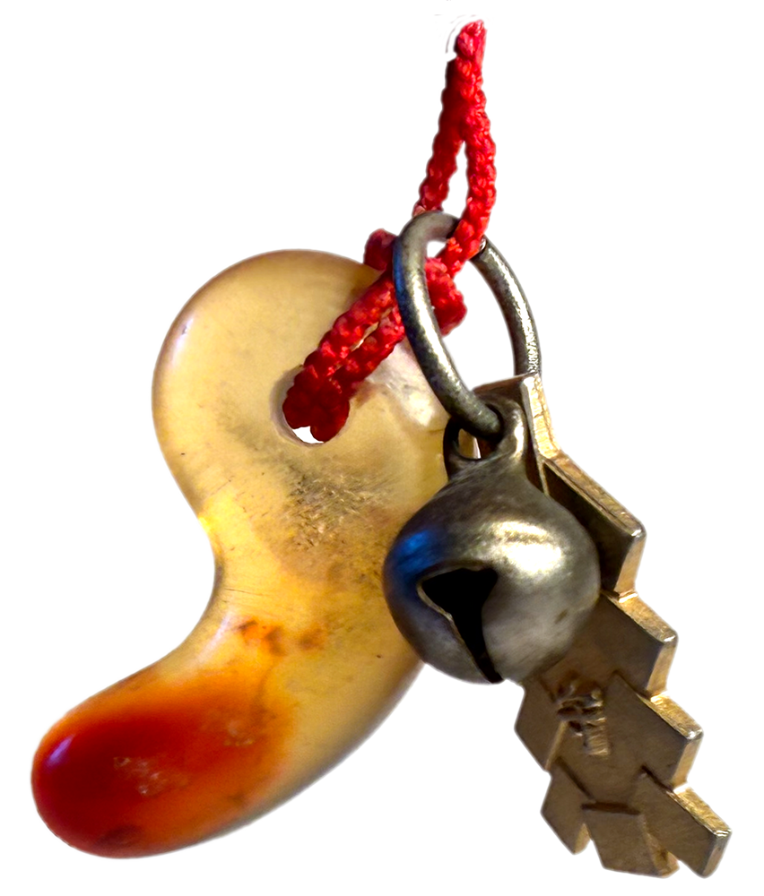 small white and red bean-shaped charm with a tiny bell and metal ribbon
